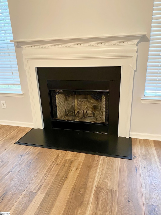 detailed view of a fireplace, wood finished floors, and baseboards