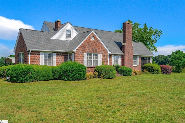 view of front of property featuring brick siding, a chimney, a front lawn, and roof with shingles