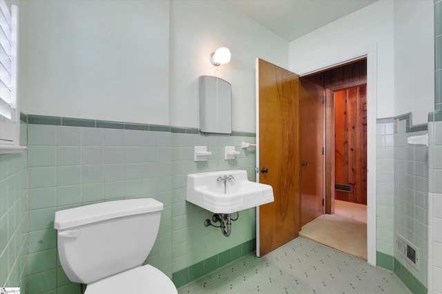 bathroom featuring tile walls, wainscoting, a sink, and toilet