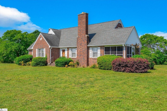 view of front of property featuring brick siding, a front yard, a sunroom, roof with shingles, and a chimney
