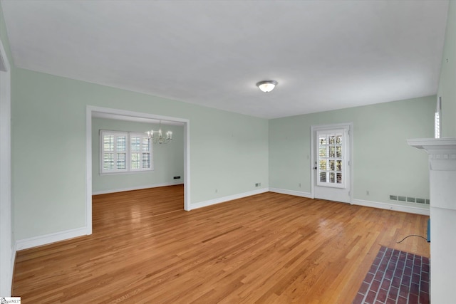 unfurnished living room with a chandelier, baseboards, and light wood-style floors
