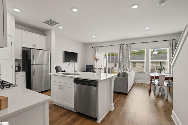 kitchen featuring appliances with stainless steel finishes, a sink, dark wood-style floors, white cabinets, and a kitchen island with sink