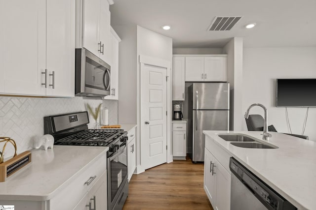 kitchen featuring appliances with stainless steel finishes, a sink, white cabinetry, light stone countertops, and tasteful backsplash