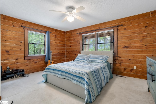 bedroom with light carpet, wood walls, a textured ceiling, and a ceiling fan