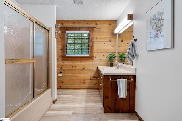 full bathroom featuring wood finished floors, vanity, shower / bath combination with glass door, a textured ceiling, and baseboards