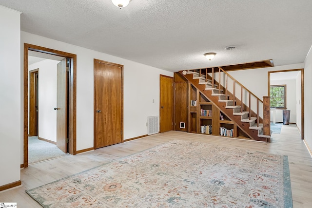 unfurnished living room featuring wood finished floors, a textured ceiling, stairs, and baseboards