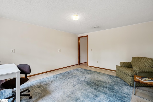 office area with light wood-style floors, baseboards, and a textured ceiling