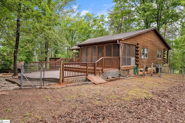 back of house featuring a sunroom, fence, log exterior, a gate, and view of scattered trees