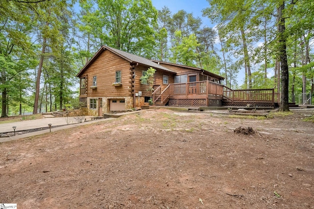 rear view of house with an attached garage, driveway, a wooden deck, and log exterior