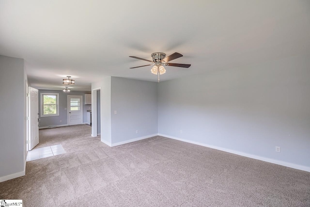 spare room with light colored carpet, a ceiling fan, and baseboards