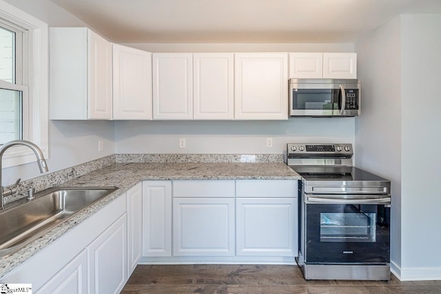 kitchen with appliances with stainless steel finishes, a sink, white cabinets, and light stone countertops