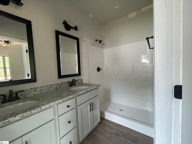 bathroom featuring walk in shower, wood finished floors, double vanity, and ceiling fan