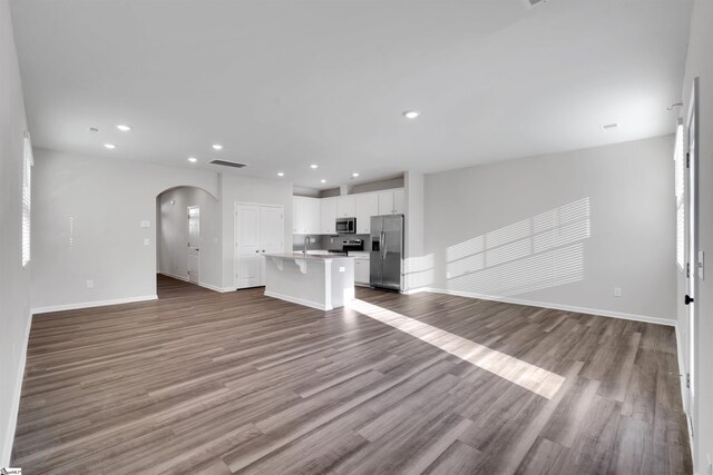 unfurnished living room with a sink, arched walkways, dark wood finished floors, recessed lighting, and baseboards