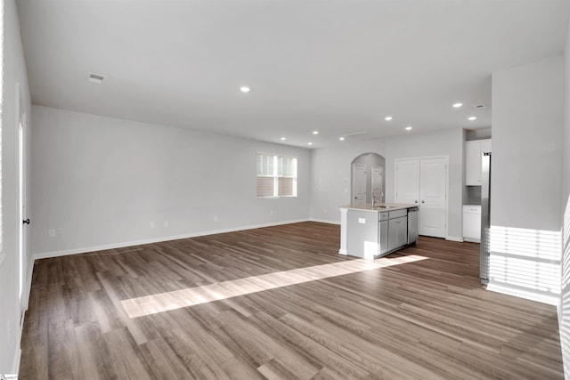 unfurnished living room with a sink, arched walkways, wood finished floors, baseboards, and recessed lighting