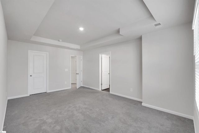 carpeted spare room featuring a raised ceiling and baseboards