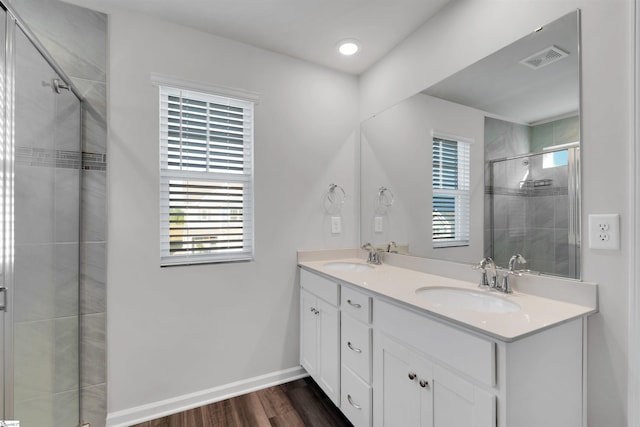 bathroom with a shower stall, wood finished floors, double vanity, and baseboards