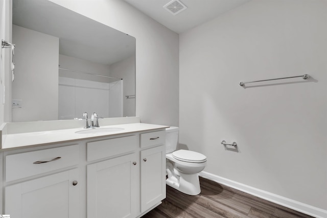 bathroom featuring toilet, baseboards, wood finished floors, vanity, and a shower