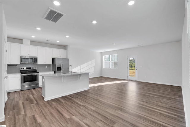 kitchen featuring stainless steel appliances, open floor plan, white cabinets, light countertops, and decorative backsplash