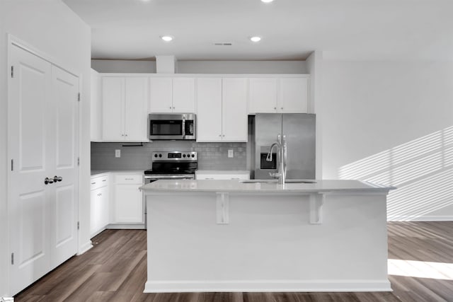 kitchen featuring appliances with stainless steel finishes, dark wood-style floors, backsplash, a sink, and a kitchen island with sink