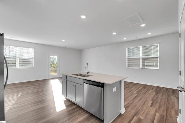 kitchen with stainless steel dishwasher, a sink, open floor plan, light countertops, and wood finished floors