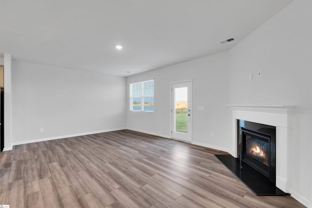 unfurnished living room with wood finished floors, a glass covered fireplace, baseboards, and recessed lighting