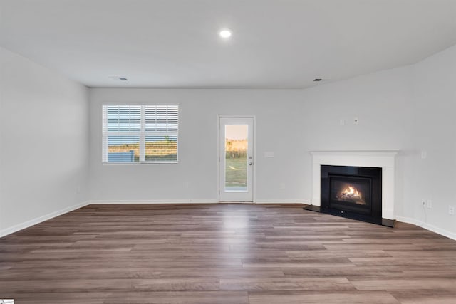 unfurnished living room featuring wood finished floors, a glass covered fireplace, baseboards, and recessed lighting