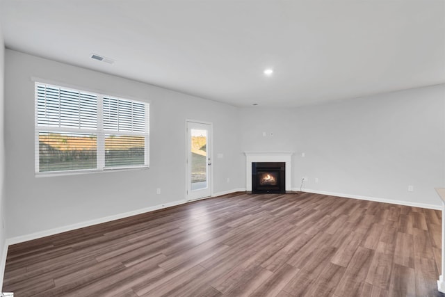 unfurnished living room featuring wood finished floors, a fireplace with flush hearth, baseboards, and recessed lighting