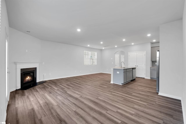 unfurnished living room featuring a sink, dark wood-style floors, recessed lighting, a glass covered fireplace, and baseboards