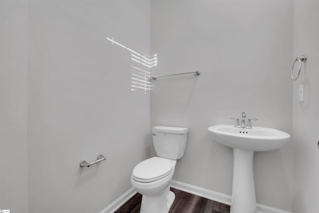 bathroom with toilet, wood finished floors, baseboards, and a sink