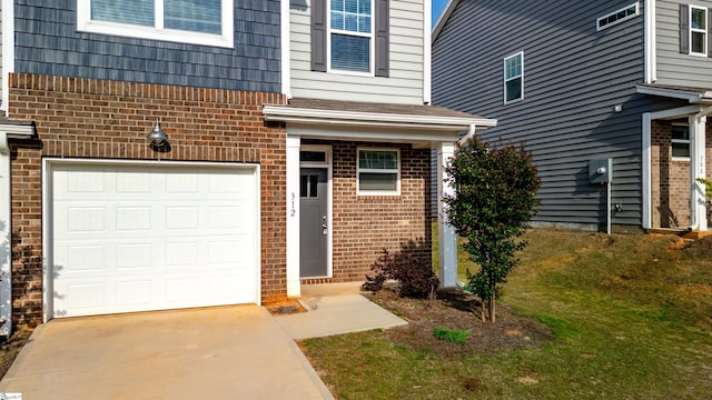 entrance to property with brick siding, a garage, driveway, and a lawn