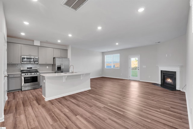 kitchen featuring stainless steel appliances, gray cabinetry, a sink, open floor plan, and light countertops