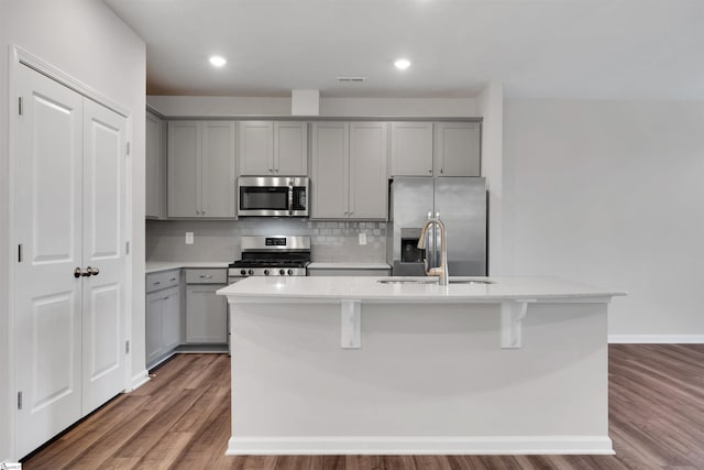 kitchen with gray cabinetry, appliances with stainless steel finishes, an island with sink, tasteful backsplash, and light countertops