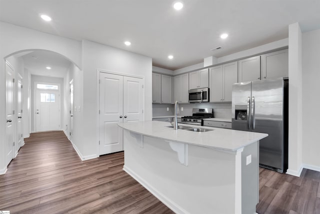 kitchen featuring stainless steel appliances, gray cabinetry, a sink, arched walkways, and recessed lighting