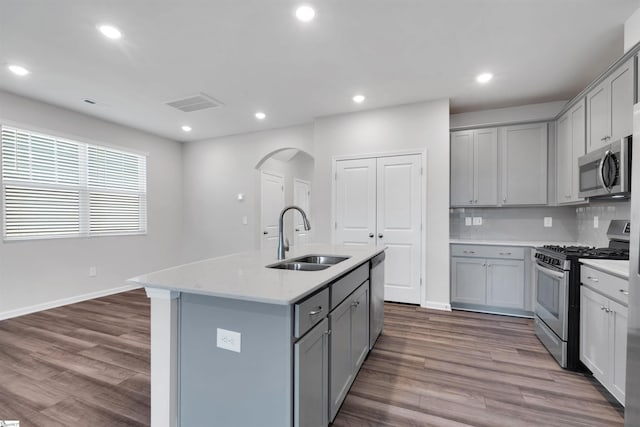 kitchen featuring appliances with stainless steel finishes, a sink, gray cabinets, dark wood-style floors, and arched walkways