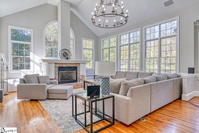 living room featuring wood finished floors, high vaulted ceiling, a chandelier, a tiled fireplace, and baseboards
