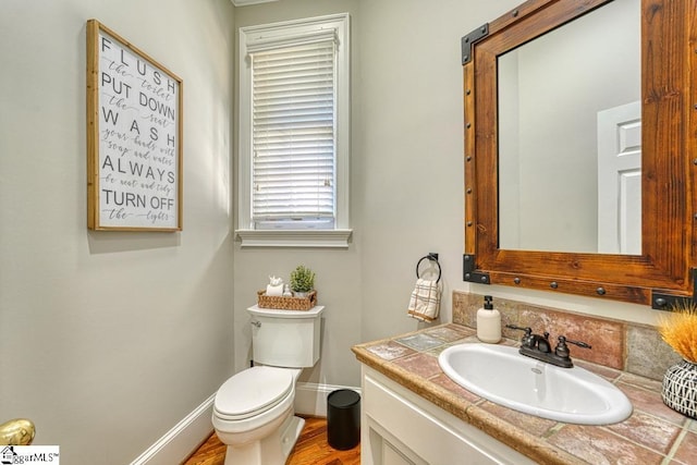 half bathroom featuring toilet, vanity, wood finished floors, and baseboards