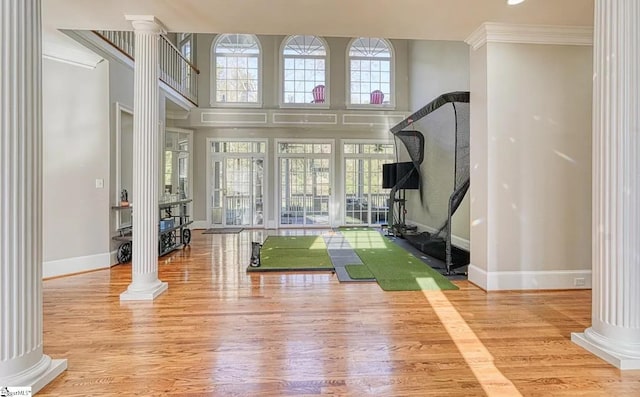 workout room featuring ornate columns, wood finished floors, baseboards, crown molding, and a towering ceiling
