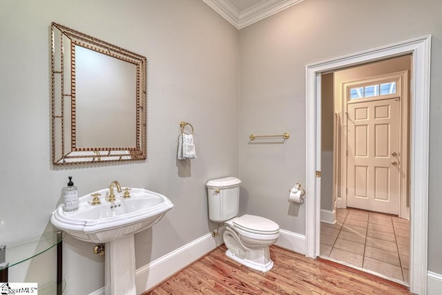 half bathroom with crown molding, baseboards, toilet, and wood finished floors