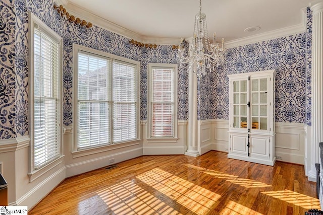 unfurnished dining area with a chandelier, light wood finished floors, wallpapered walls, ornamental molding, and a wainscoted wall