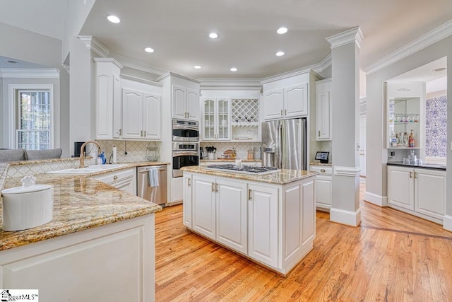 kitchen with stainless steel appliances, a sink, crown molding, light wood-style flooring, and backsplash