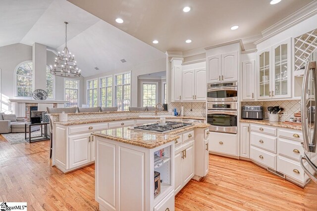 kitchen featuring stainless steel appliances, healthy amount of natural light, vaulted ceiling, white cabinets, and glass insert cabinets