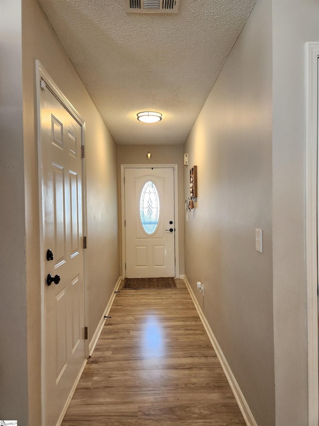 doorway featuring a textured ceiling, wood finished floors, and baseboards