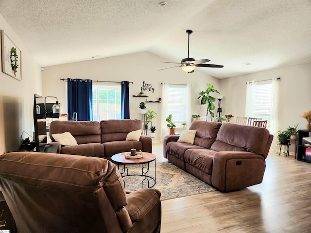 living area featuring a textured ceiling, lofted ceiling, healthy amount of natural light, a ceiling fan, and light wood-type flooring