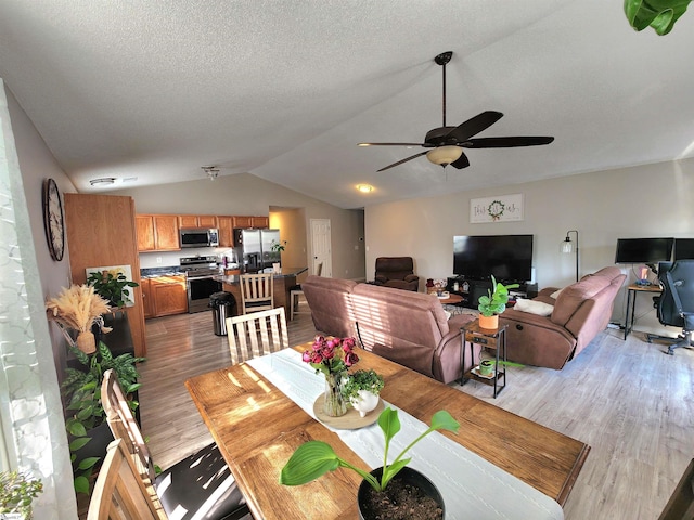 dining room featuring light wood-style floors, vaulted ceiling, and ceiling fan