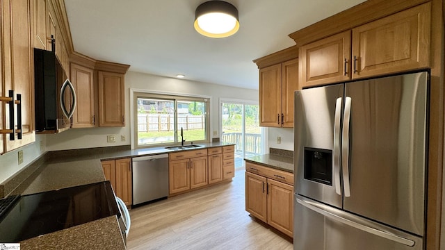 kitchen featuring appliances with stainless steel finishes, a sink, light wood-style floors, dark stone countertops, and brown cabinetry