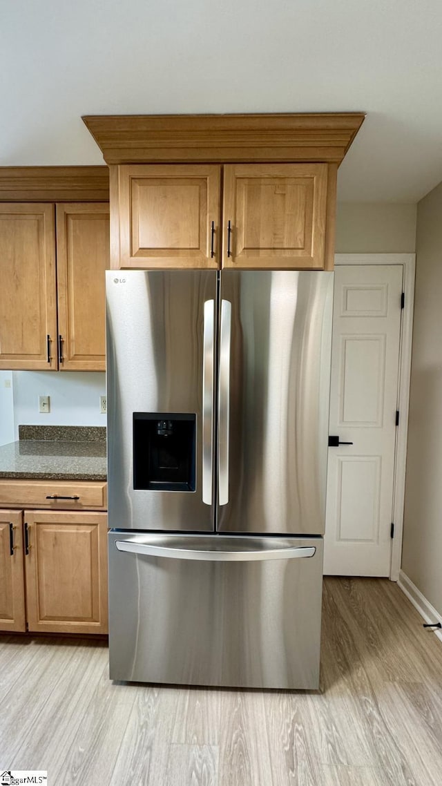 kitchen featuring stainless steel fridge, light wood finished floors, dark stone counters, and brown cabinetry