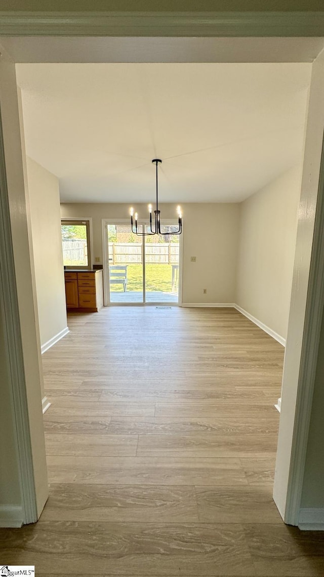 unfurnished dining area with a chandelier, baseboards, light wood-style floors, and healthy amount of natural light