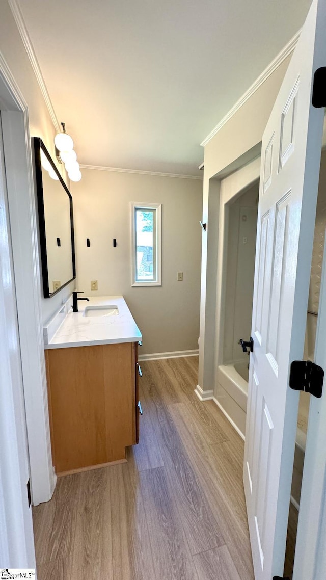 full bathroom featuring wood finished floors, ornamental molding, double vanity, a tub, and baseboards