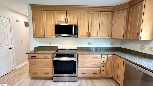 kitchen with stainless steel appliances, light wood finished floors, and dark stone counters