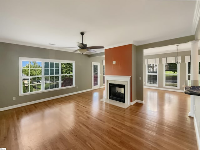 unfurnished living room featuring wood finished floors, a fireplace with flush hearth, baseboards, a ceiling fan, and crown molding